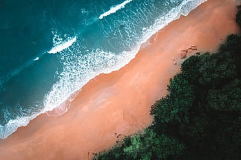 Breathtaking aerial view of waves crashing on a sandy beach, surrounded by lush greenery. HD wallpaper