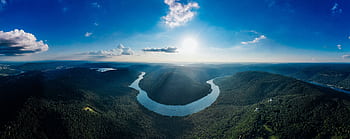 Stunning aerial view of a lush river bend surrounded by mountains under a bright blue sky. HD wallpaper