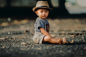 Adorable toddler boy wearing a hat and sitting on the ground in a natural setting. HD wallpaper