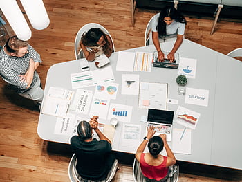 A diverse group working on marketing strategies with charts and laptops in an office setting. HD wallpaper