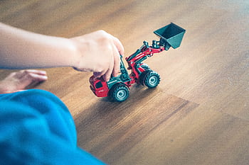 A child plays with a toy excavator on a wooden floor, enjoying creative indoor playtime. HD wallpaper