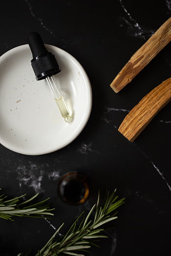 A soothing flat lay composition featuring aromatic oils and rosemary on a dark surface. HD phone wallpaper