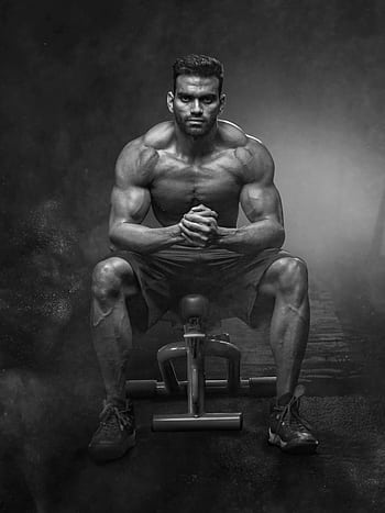 A powerful bodybuilder sitting with intense focus, showcasing muscular definition and strength. HD phone wallpaper