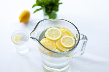 Top-down view of lemon slices in a glass pitcher filled with water, offering a refreshing drink option. HD wallpaper