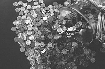Monochrome of coins spilling from a glass jar, symbolizing wealth and savings. HD wallpaper