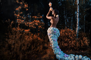 Captivating of a woman adorned with flowers posing elegantly in an autumn forest. HD wallpaper