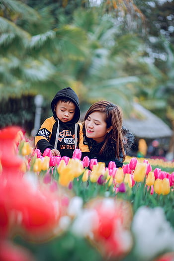 A happy mother and child enjoying colorful tulips in a garden during daytime. HD phone wallpaper