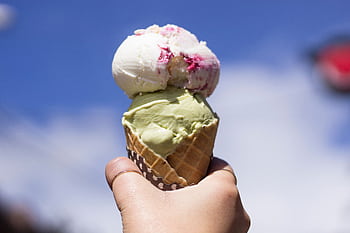 Hand holding a delicious double scoop ice cream cone against a bright blue sky. HD wallpaper