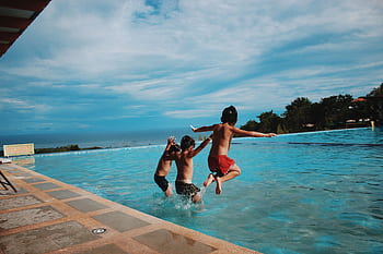 Two children joyfully jump into a pool on a sunny day, embodying excitement and summer vibes. HD wallpaper