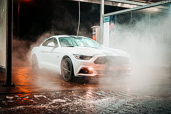White Ford Mustang in a misty carwash setting, illuminated at night in an urban environment. HD wallpaper