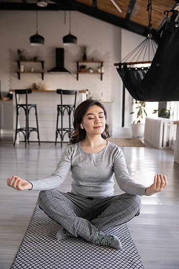 A woman meditates peacefully on a yoga mat indoors, promoting mindfulness and relaxation. HD phone wallpaper