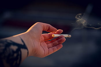 A tattooed hand holding a smoking cigarette, captured in a close-up with shallow focus. HD wallpaper