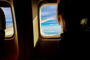 Silhouette of a woman looking out an airplane window at clouds and blue sky. HD wallpaper