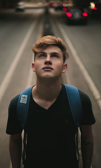 Portrait of a young man looking up in a city street with blurred traffic background. HD phone wallpaper