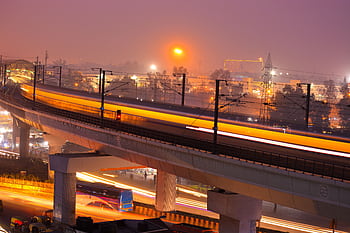 Dynamic night view of a modern city with illuminated train tracks showcasing speed and urban life. HD wallpaper