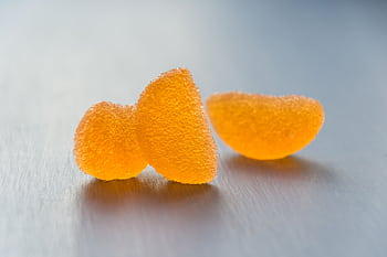 Bright macro shot showcasing textured orange jelly candies on a sleek surface. HD wallpaper
