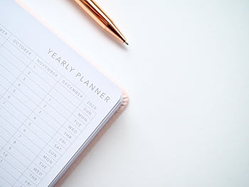 A stylish yearly planner open to a 2020 calendar page, accompanied by a golden pen on a clean white surface. HD wallpaper