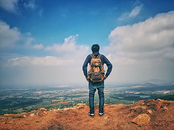 A man stands on a mountain edge appreciating the expansive scenic view below under a bright sky. HD wallpaper