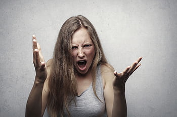 A young woman showing intense anger and frustration, yelling with hands raised against a gray background. HD wallpaper