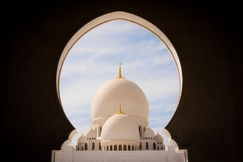 Captivating view of white domes of Sheikh Zayed Grand Mosque through an archway against the blue sky. HD wallpaper
