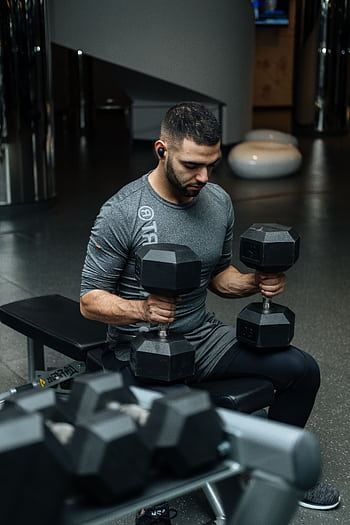 Adult man lifting dumbbells in a gym, focused on strength training workout. HD phone wallpaper