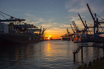 Shipping vessels at Hamburg port during a vibrant sunset, showcasing industrial cranes. HD wallpaper