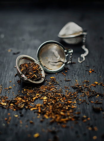 Loose dried tea leaves scattered with a metal tea strainer on a dark surface. HD phone wallpaper