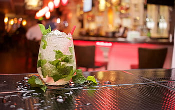 Close-up of a mojito cocktail with crushed ice and mint leaves on a bar counter, perfect for nightlife and refreshment themes. HD wallpaper