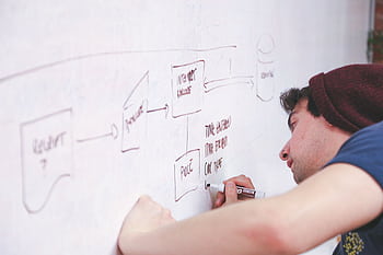 A young adult sketches a project flow on a whiteboard, showcasing creativity and planning. HD wallpaper