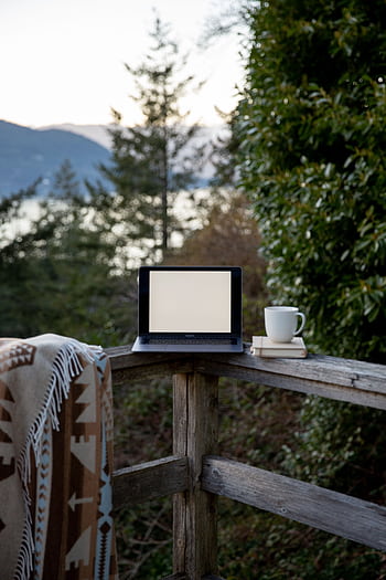 Tranquil outdoor setting with laptop and coffee cup on a rustic wooden balcony overlooking nature. HD phone wallpaper