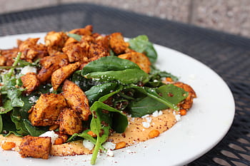 Delicious chicken salad with spinach, feta cheese, and creamy sauce on a white plate. HD wallpaper