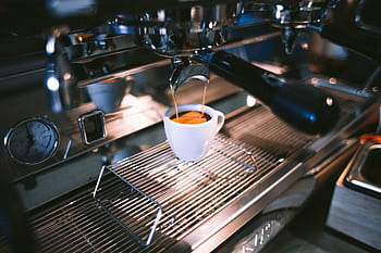 Close-up view of espresso being brewed into a cup using a professional coffee machine in a café. HD wallpaper