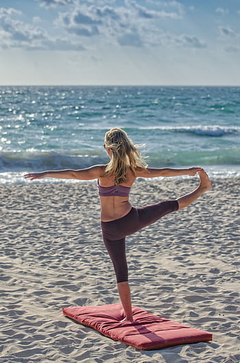 A woman performs yoga on a sandy beach at sunrise, embracing wellness and tranquility. HD phone wallpaper
