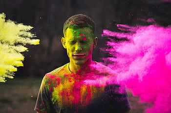 A man covered in vibrant powder during a Holi festival celebration outdoors. HD wallpaper