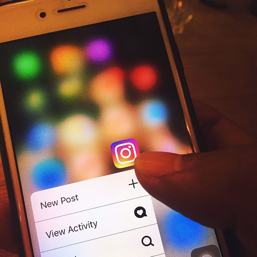 Finger navigating Instagram app on a smart screen with colorful blurred background. HD phone wallpaper