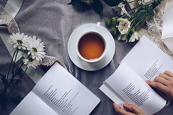 Inviting cozy reading setup with tea, poetry books, and fresh flowers on a table. HD wallpaper
