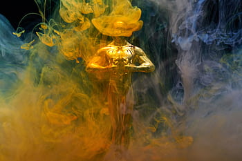 A golden statuette enveloped in vibrant yellow and blue smoke, symbolizing achievement and success. HD wallpaper