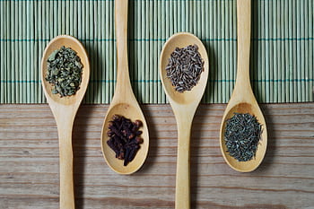 Overhead view of wooden spoons filled with spices and herbs on a bamboo mat, ideal for culinary themes. HD wallpaper