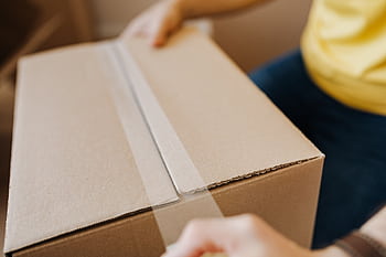 Close-up of a person sealing a cardboard box with tape, suggesting relocation or delivery. HD wallpaper