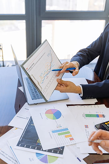 Business professionals discussing financial graphs and charts in an office setting. HD phone wallpaper