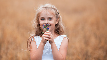 Smiling Cute Little Girl With Blue Flowers Is Standing In Blur Background Wearing White Dress Cute HD wallpaper