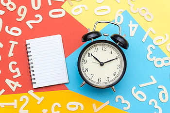 A flat lay of a classic alarm clock with a blank notebook on a colorful background surrounded by numbers. HD wallpaper