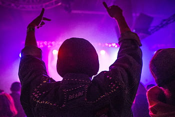 Back view of a person enjoying an energetic nightclub scene with vibrant neon lights and music. HD wallpaper