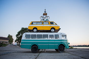 Creative outdoor sculpture featuring a van stacked on a bus with a bicycle on top. HD wallpaper