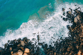 A stunning aerial view of ocean waves crashing on a rocky shore, capturing nature's raw beauty. HD wallpaper