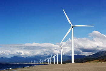A row of wind turbines on a sandy coastline under a clear blue sky, promoting renewable energy. HD wallpaper