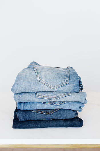 Collection of neatly folded denim jeans in various shades of blue on a white table. HD phone wallpaper