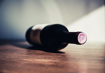 Close-up of a wine bottle on a wooden table, showcasing elegant shadows and soft lighting. HD wallpaper