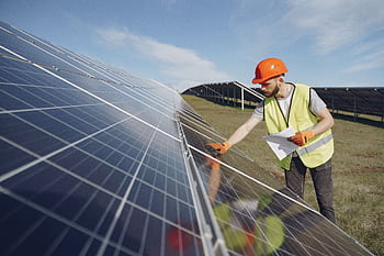 Technician in PPE inspects solar panels in a renewable energy field, promoting sustainability. HD wallpaper