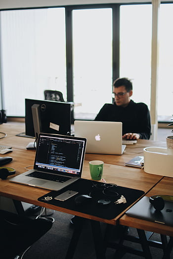A web developer working on code in a modern office setting with multiple devices. HD phone wallpaper